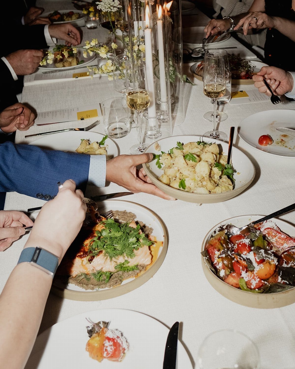 15 Small Wedding Ideas for 50 Guests, From Backyards to Parks 1 Communal bowls of food and salmon plates on a white wedding reception table.