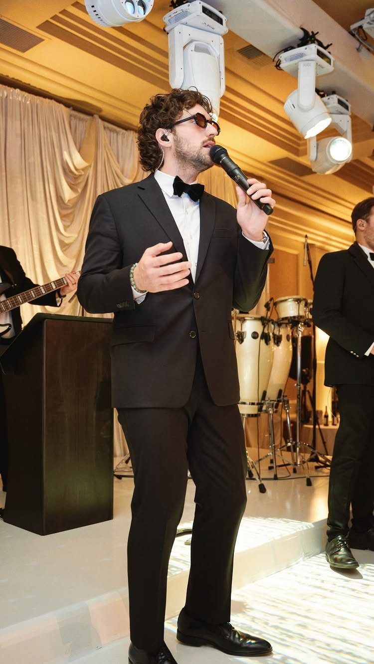 15 Small Wedding Ideas for 50 Guests, From Backyards to Parks 2 Male singer in a tuxedo performing with a microphone on a white stage