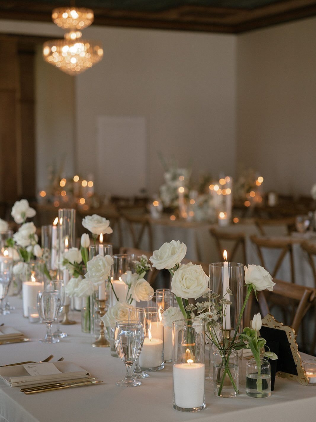 15 Small Wedding Ideas for 50 Guests, From Backyards to Parks 7 Long wedding table with white roses and glowing candles in a dim room.