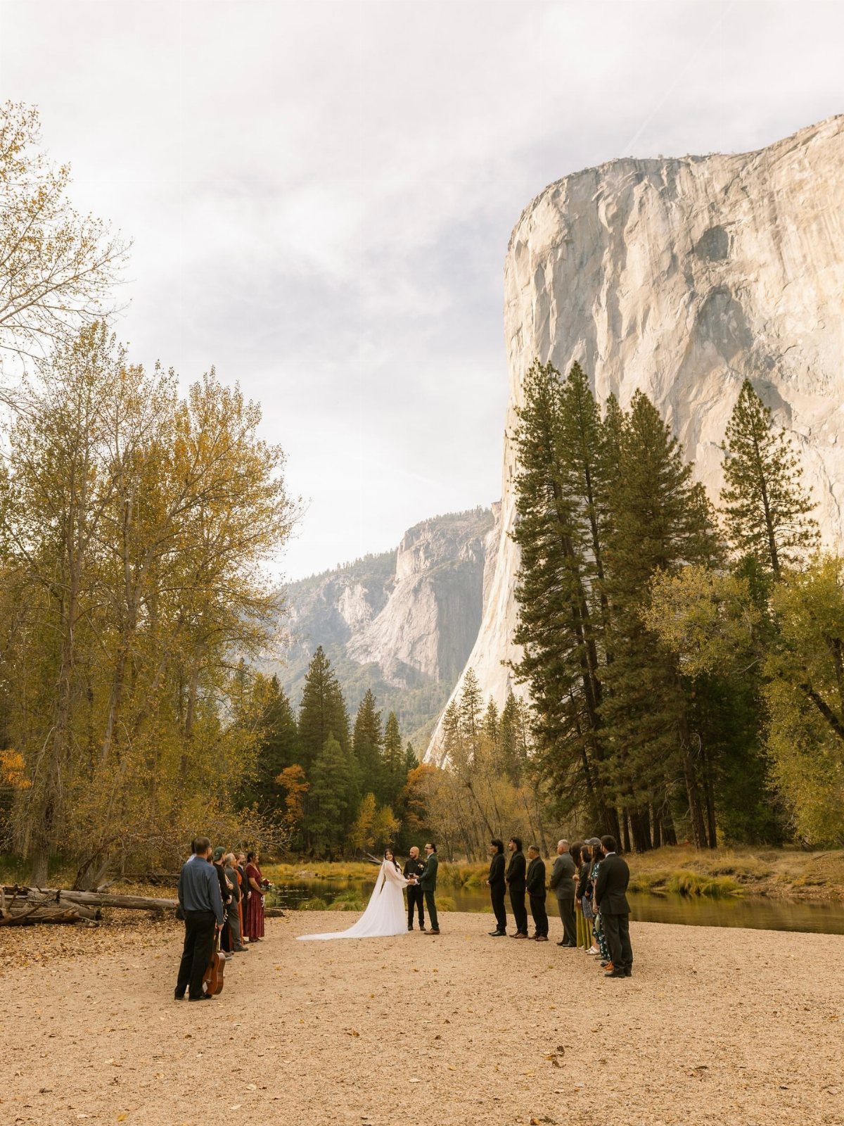 15 Small Wedding Ideas for 50 Guests, From Backyards to Parks 5 Wedding ceremony on a sandy riverbank with a massive granite cliff and pine trees.