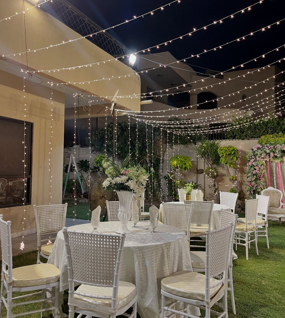 13 Small Wedding Party Ideas for an Intimate Celebration 10 White wedding tables and chairs on a lawn under strings of fairy lights.