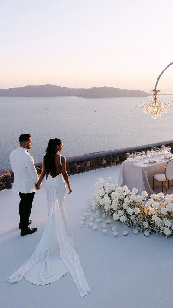 13 Small Wedding Party Ideas for an Intimate Celebration 11 Bride and groom holding hands on a white terrace overlooking a scenic ocean view.