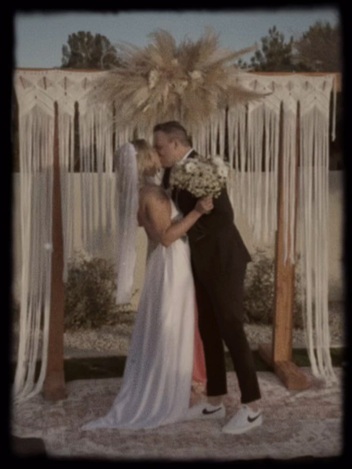 13 Small Wedding Party Ideas for an Intimate Celebration 7 Bride and groom kissing under a macrame and pampas grass wedding arch outdoors.