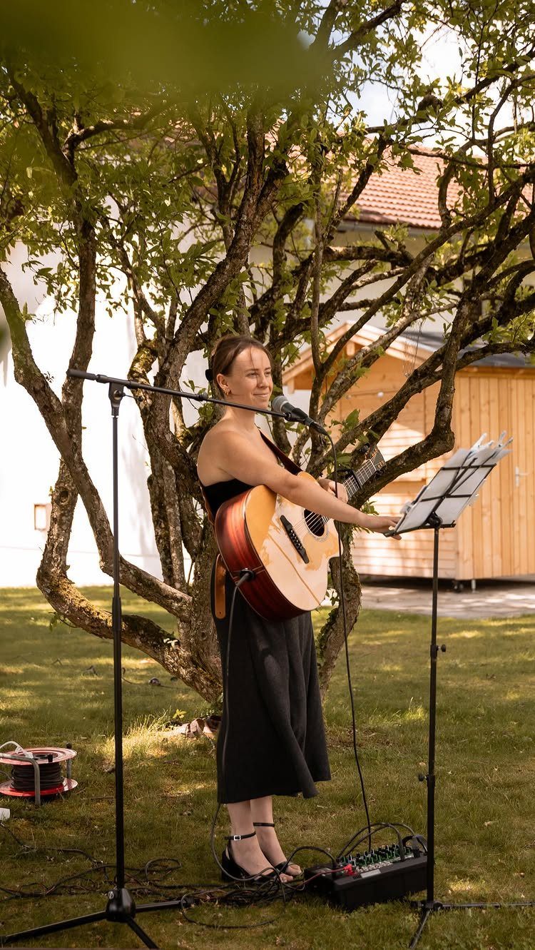 13 Small Wedding Party Ideas for an Intimate Celebration 8 Woman playing acoustic guitar and singing into a microphone under a tree outdoors.