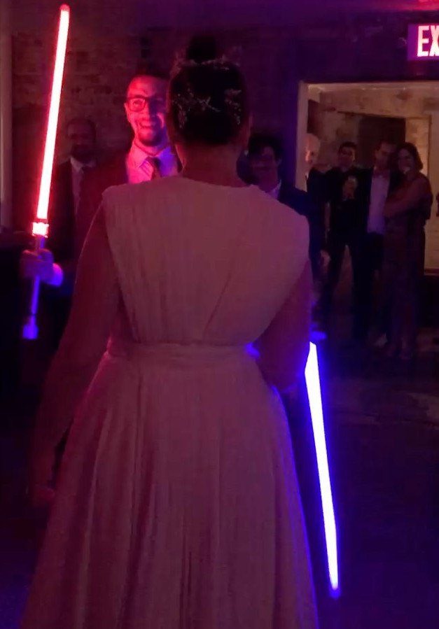 Bride in white dress and groom with lightsabers at a themed wedding reception