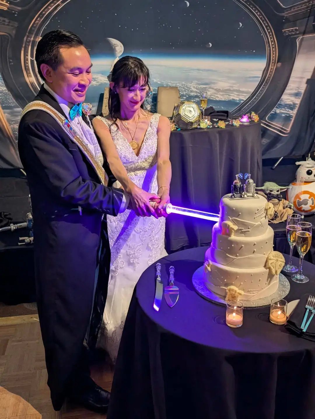 Bride and groom cutting a wedding cake with a blue lightsaber in space setting