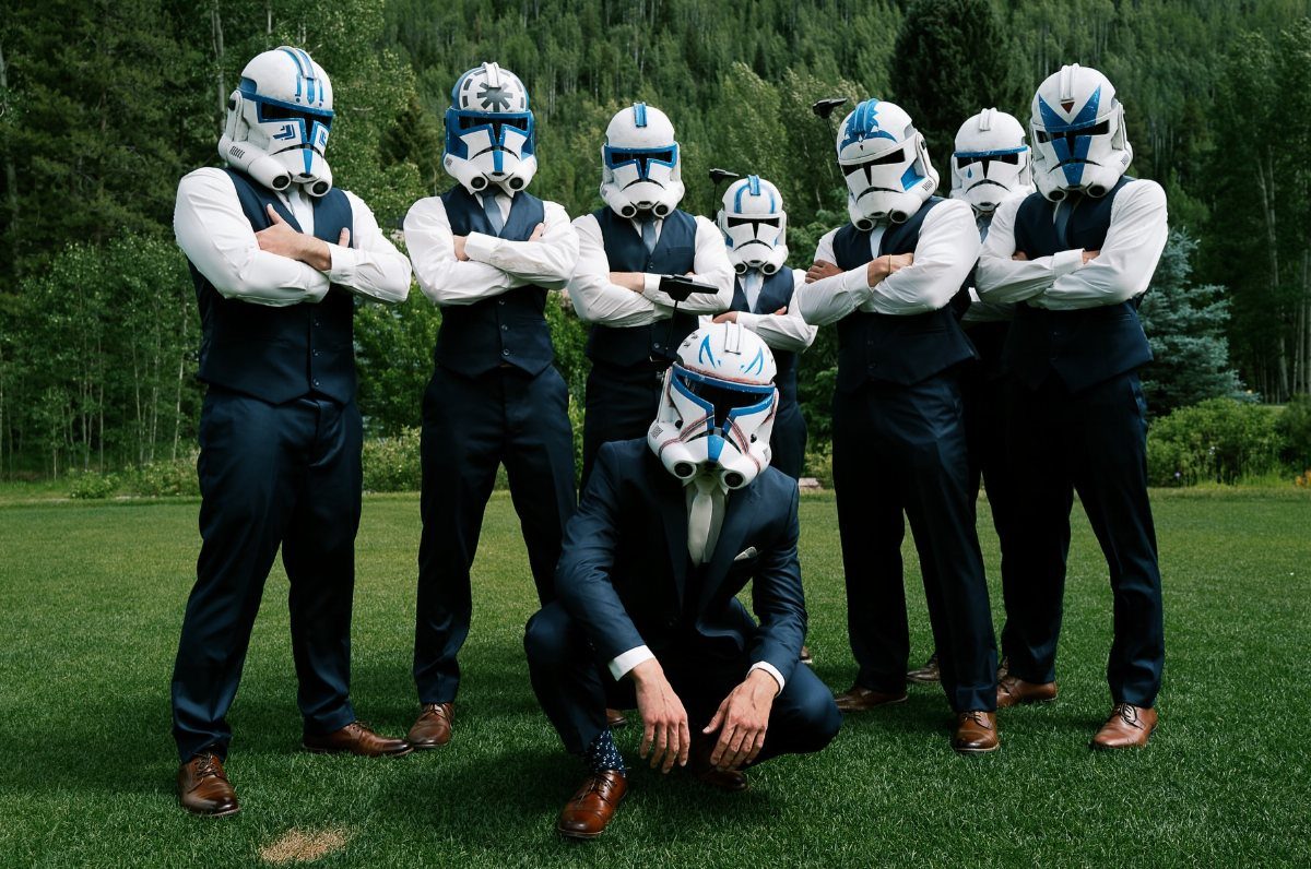 Men in navy suits wearing clone trooper helmets posing on a green lawn.