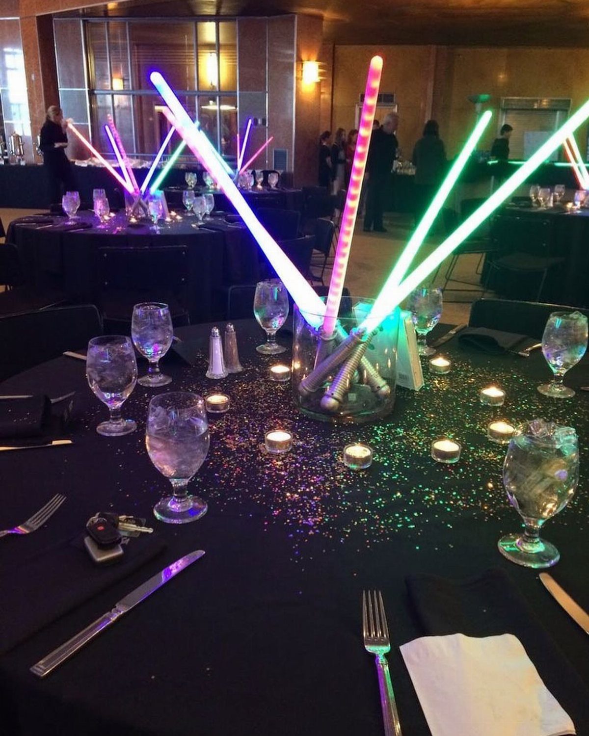 Glowing lightsabers in a vase as a centerpiece on a black wedding banquet table.