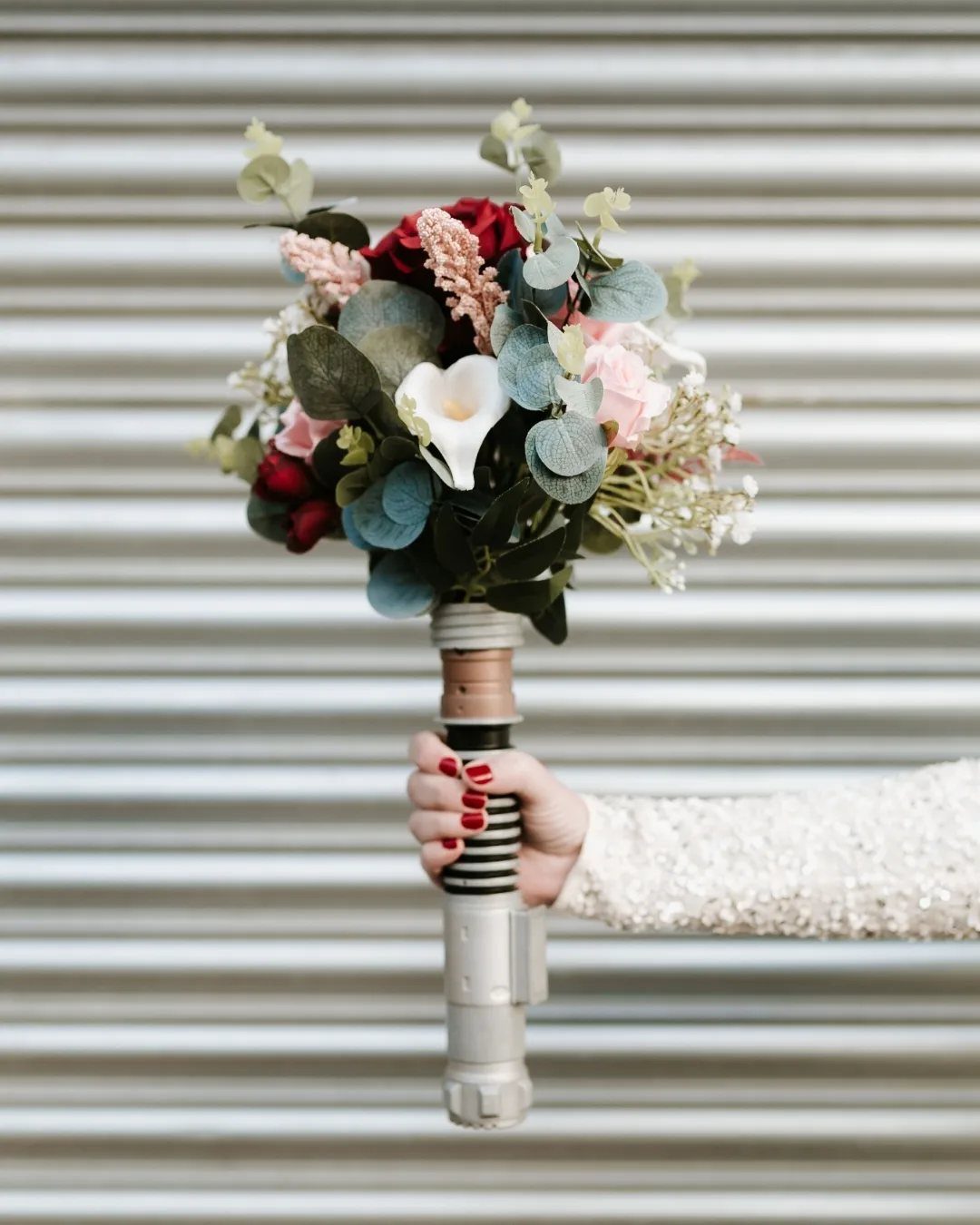 Bridal bouquet with red and white flowers featuring a lightsaber hilt as the handle.