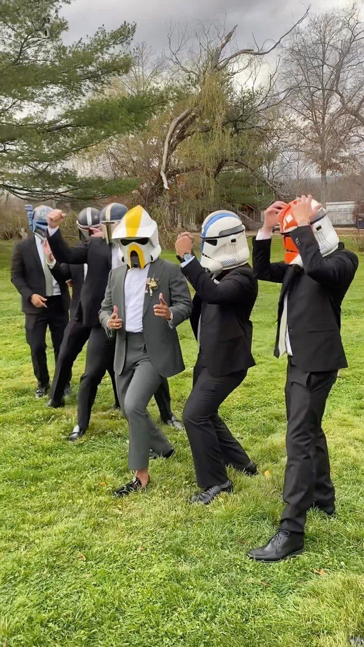 Men in formal suits wearing Star Wars clone trooper helmets posing in a field