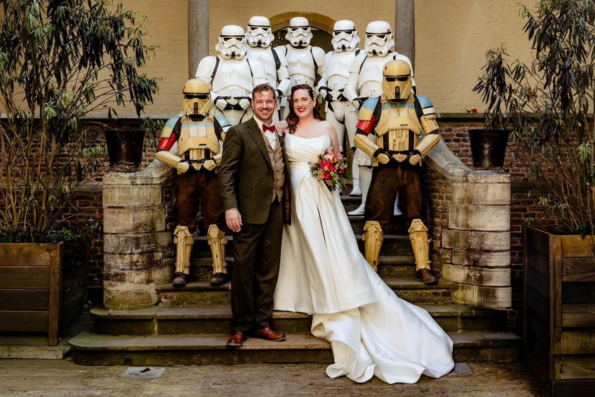 Bride and groom posing on stone steps surrounded by Star Wars Stormtroopers