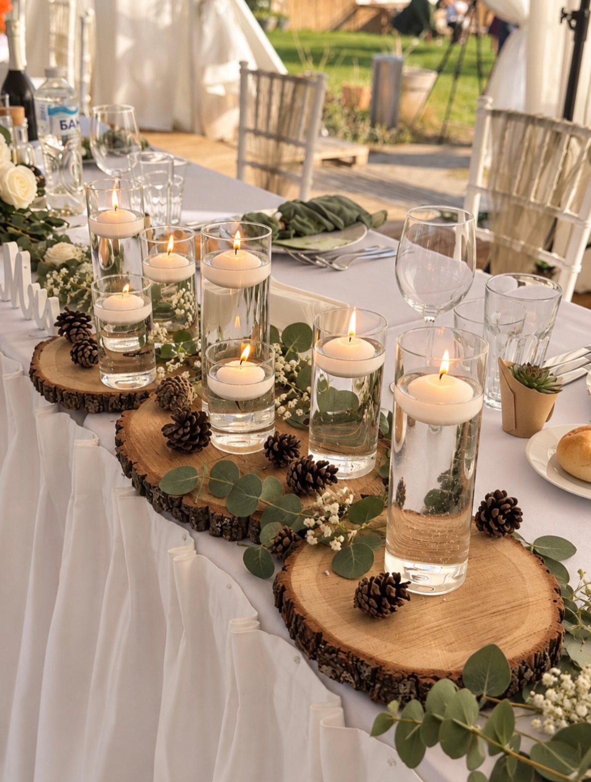 16 Tent Wedding Ideas for Lighting, Tables and Cozy Corners 15 Floating white candles in glass cylinders on wooden slices with pinecones and greenery.