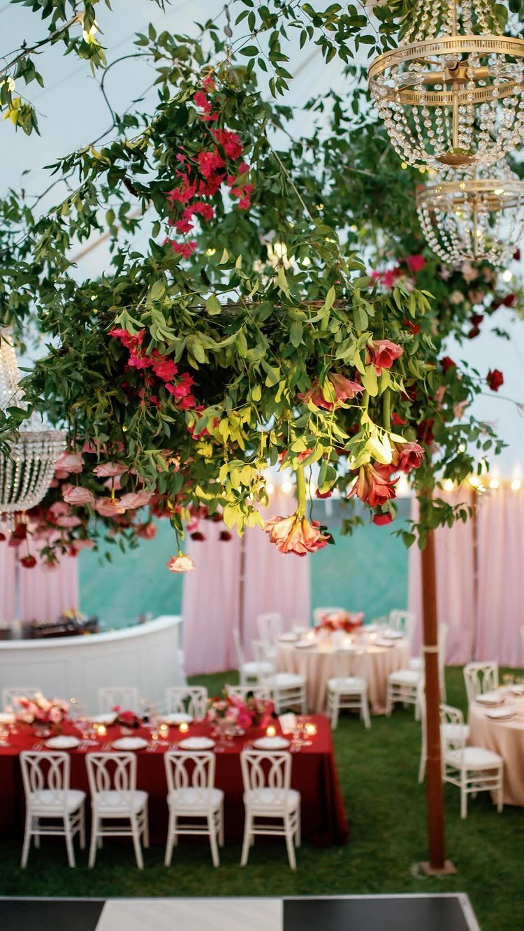 16 Tent Wedding Ideas for Lighting, Tables and Cozy Corners 14 Wedding tent interior with red table settings under a floral canopy and chandeliers.