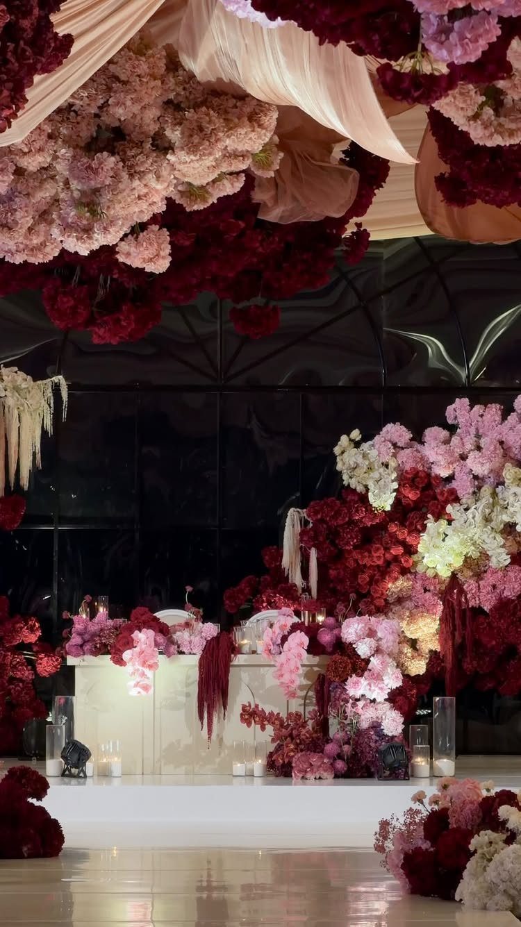 16 Tent Wedding Ideas for Lighting, Tables and Cozy Corners 1 Floral canopy of pink and burgundy flowers with draped cream fabric over a wedding table.