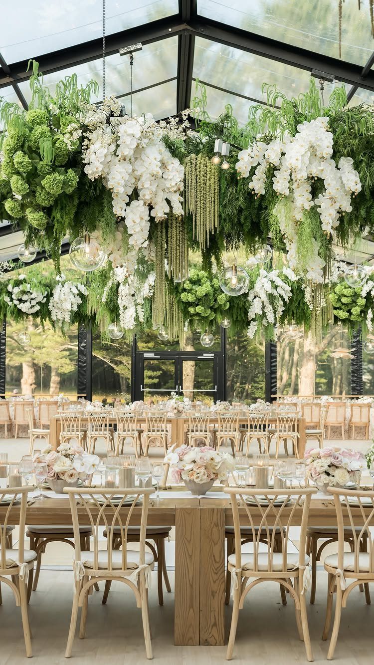 16 Tent Wedding Ideas for Lighting, Tables and Cozy Corners 4 Lush hanging greenery and white flowers suspended above wooden wedding tables in a glass tent.