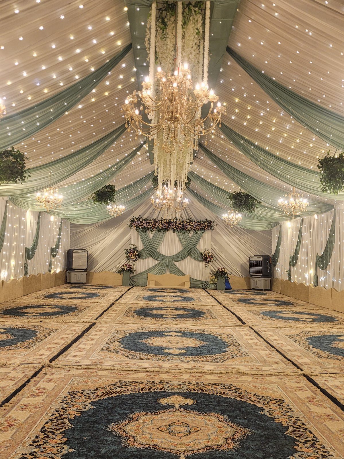 16 Tent Wedding Ideas for Lighting, Tables and Cozy Corners 11 Wedding tent interior with draped fabric, chandeliers, string lights, and patterned floor rugs.
