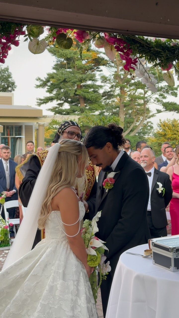 Bride and groom standing under a floral arch during their outdoor wedding ceremony.