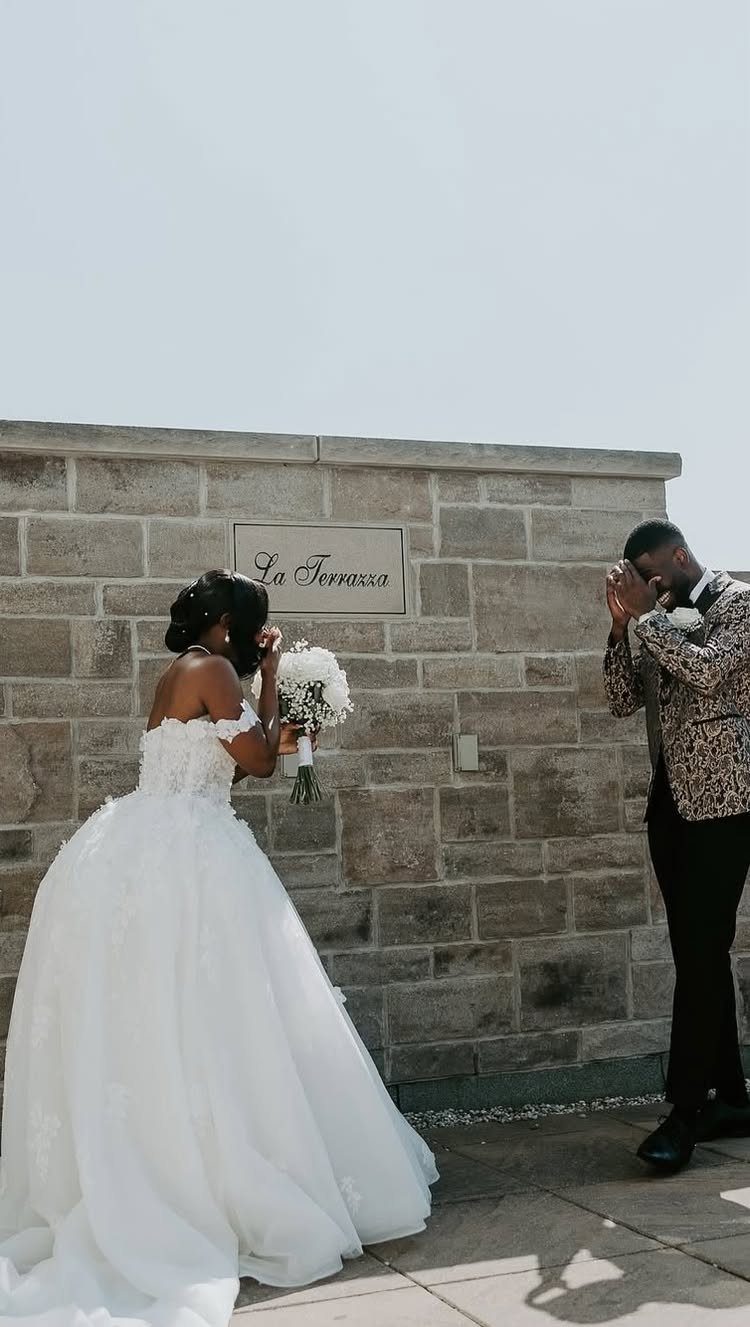 Bride and groom sharing a private first look moment against a stone wall.