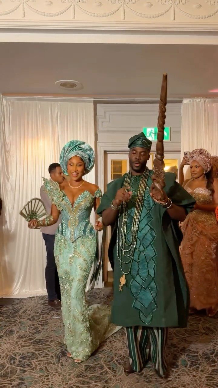 Couple in traditional green Nigerian wedding attire entering a reception room together.