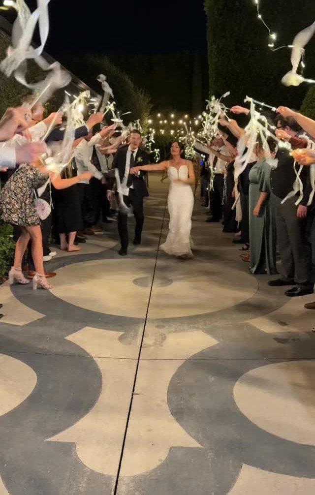 Bride and groom walking through a celebratory arch of white ribbons at night.