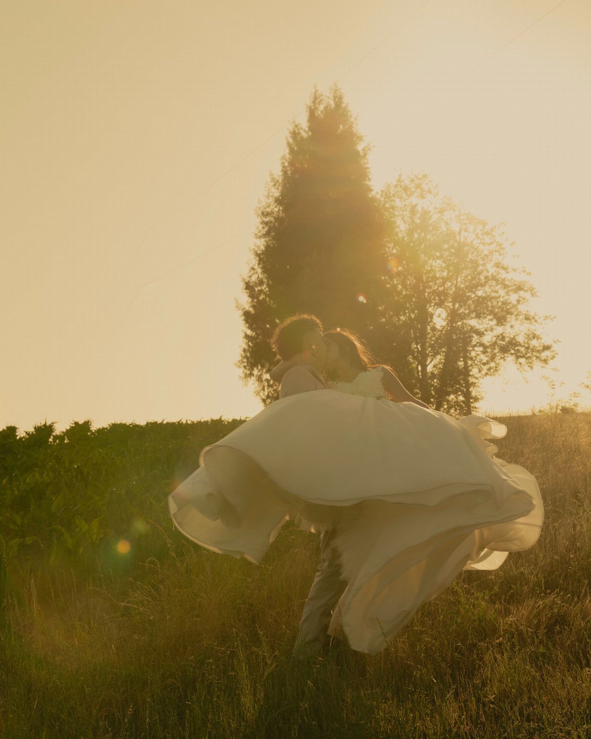 Groom carrying bride in a white dress during a golden hour sunset kiss.