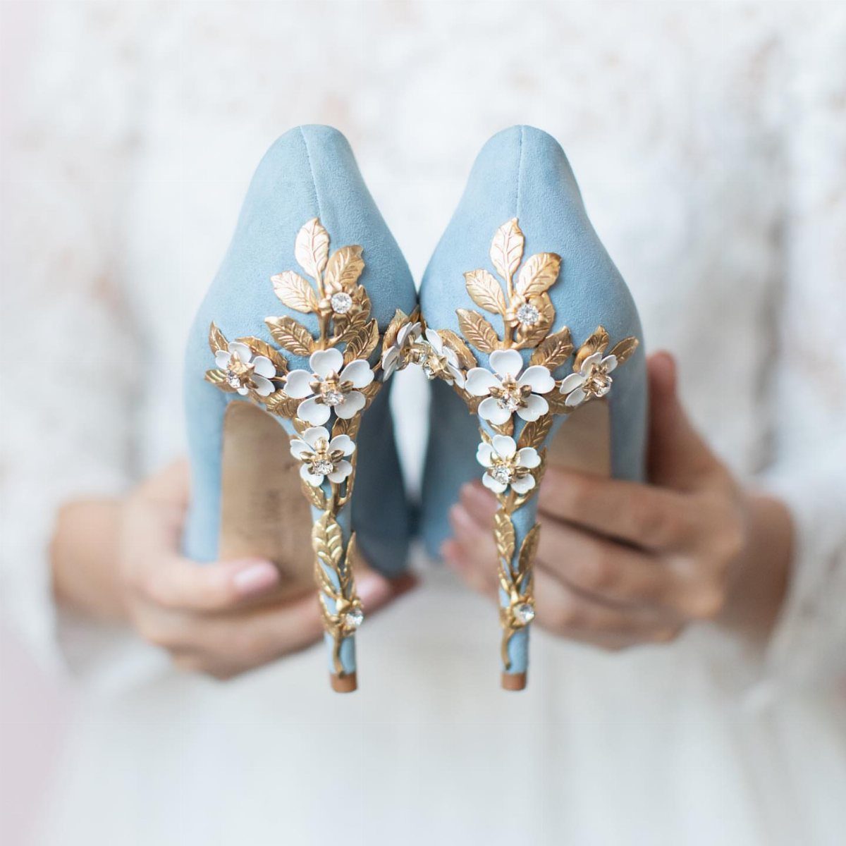 9 Uncommon Wedding Colors for Couples Who Skip the Usual 7 Dusty blue high heels with gold floral embellishments held against a white lace dress.
