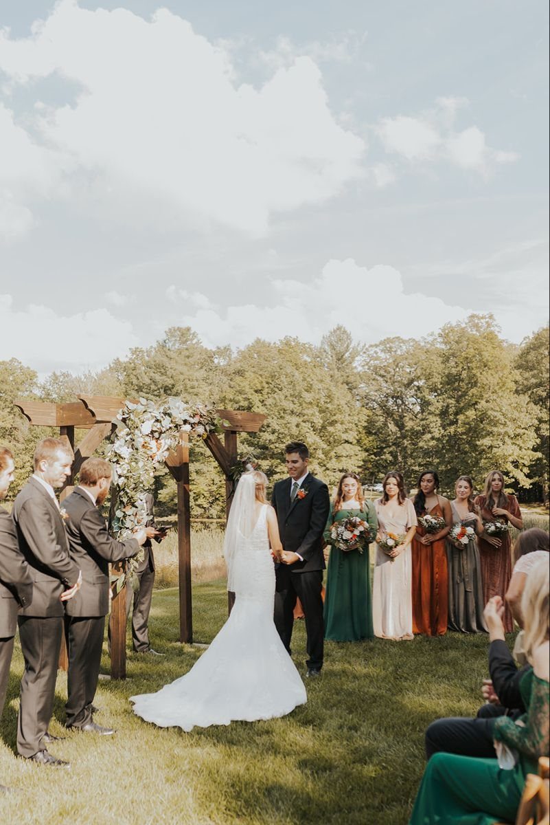 Bride and groom under a floral arch with an uneven number of attendants.