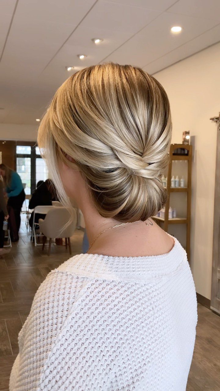Blonde hair styled in a classic low chignon bun with a white sweater.