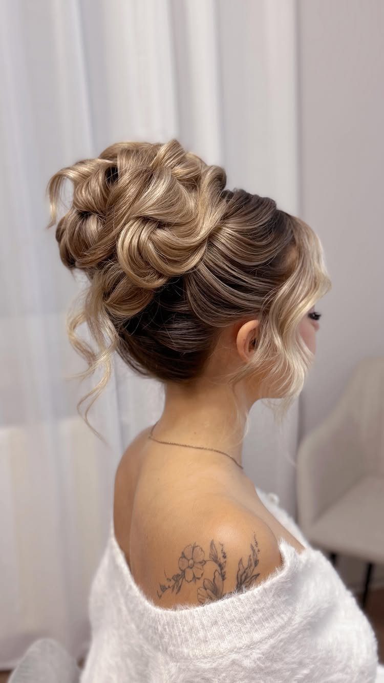 Voluminous high bun with loose curled strands framing a woman's face and neck.
