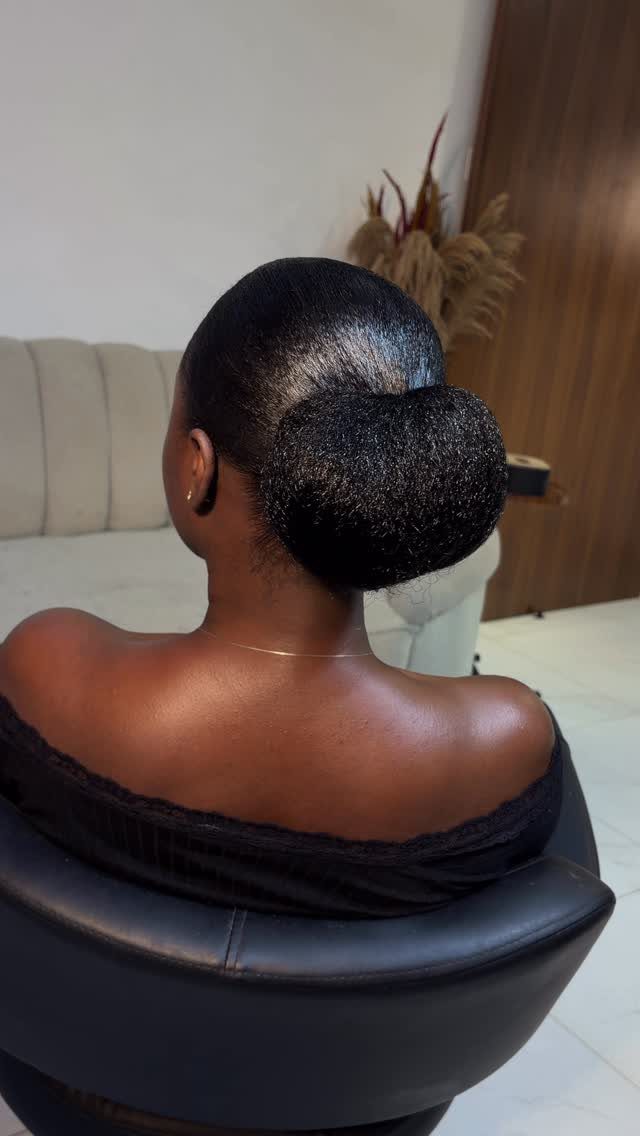 Sleek low bun hairstyle on a person with dark hair wearing black clothing.