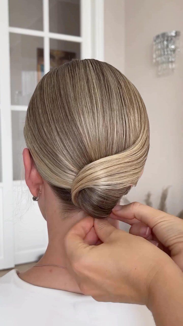 Sleek low bun on blonde hair being adjusted by hands at the nape.