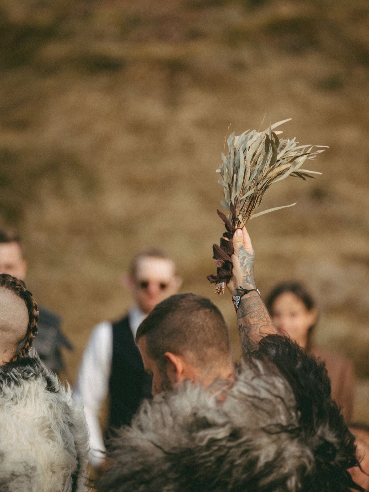 Man in grey fur cloak holding dried herbs aloft at a themed event