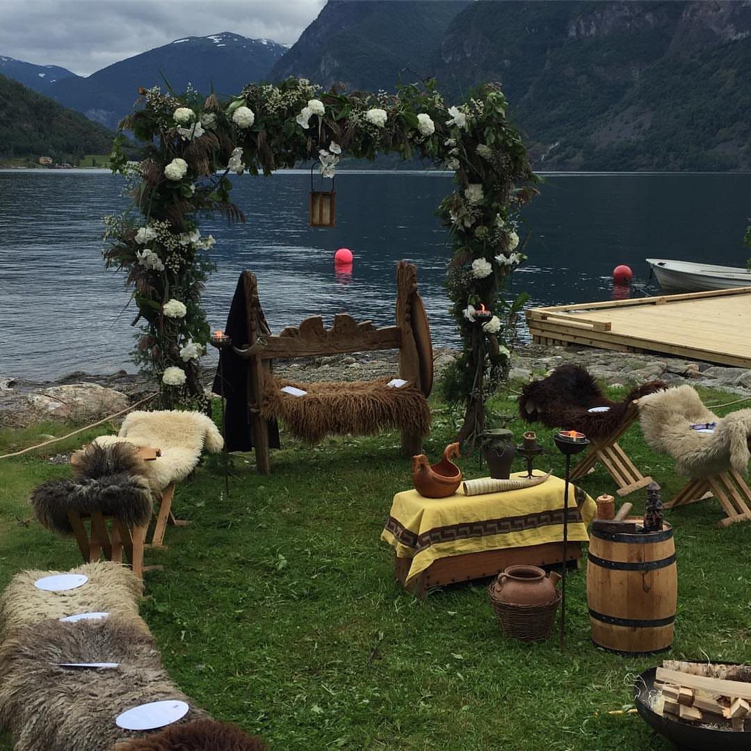 Floral wedding arch and carved wooden thrones with furs by a mountain lake.