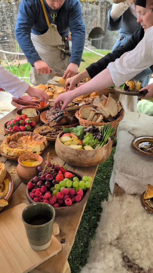 Rustic Viking feast with meats, fruits, and breads on a wooden table outdoors.