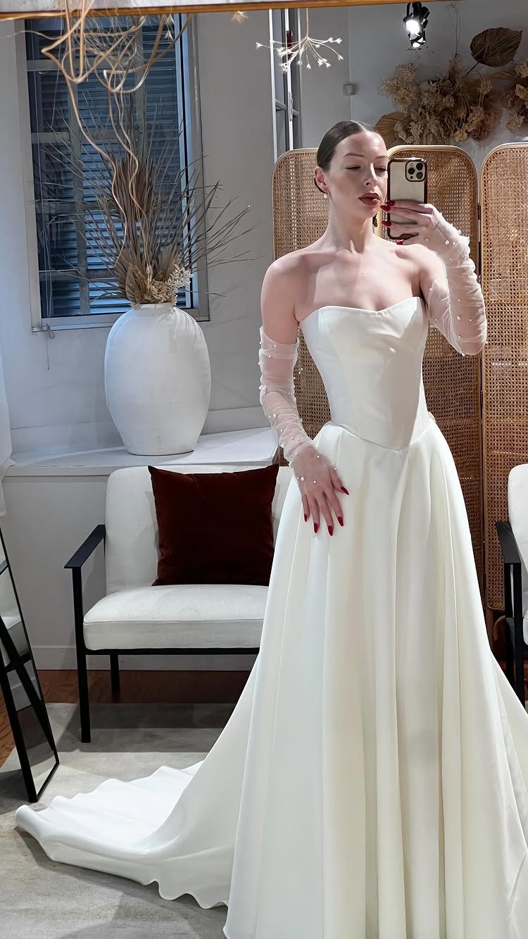 9 Ideas for a Vintage Basque Waist Wedding Dress 9 Woman in a white strapless wedding dress with a basque waist and sheer sleeves.