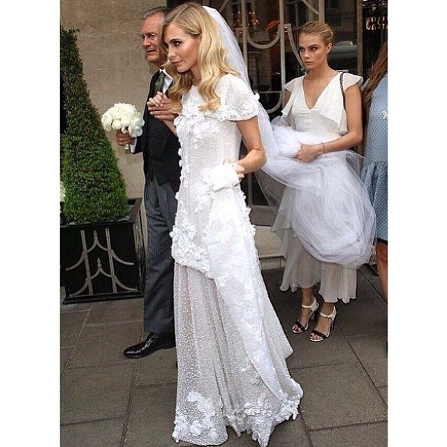 Vintage Chanel Wedding Dress Ideas: 8 Bridal Looks 8 Woman in a white floral lace wedding dress and veil walking outdoors.