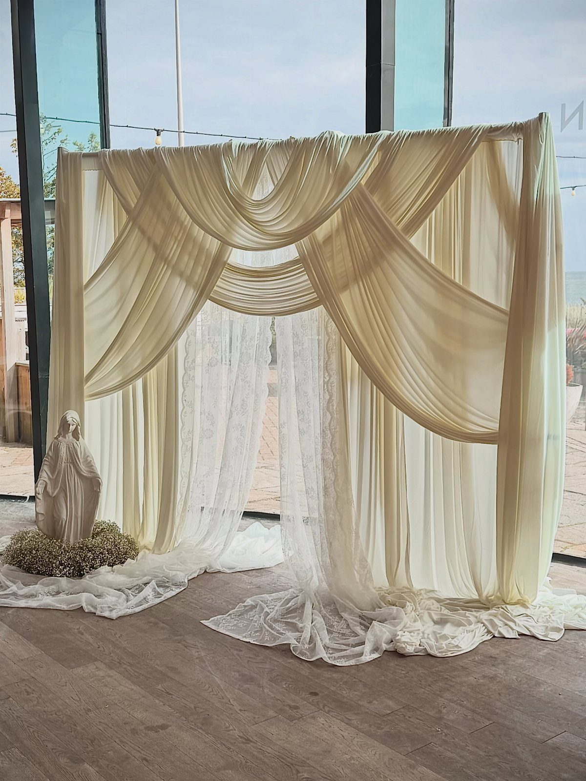 5 Wedding Arch Without Flowers Ideas for Your Ceremony 1 Cream fabric draped backdrop with lace accents and a small white statue.