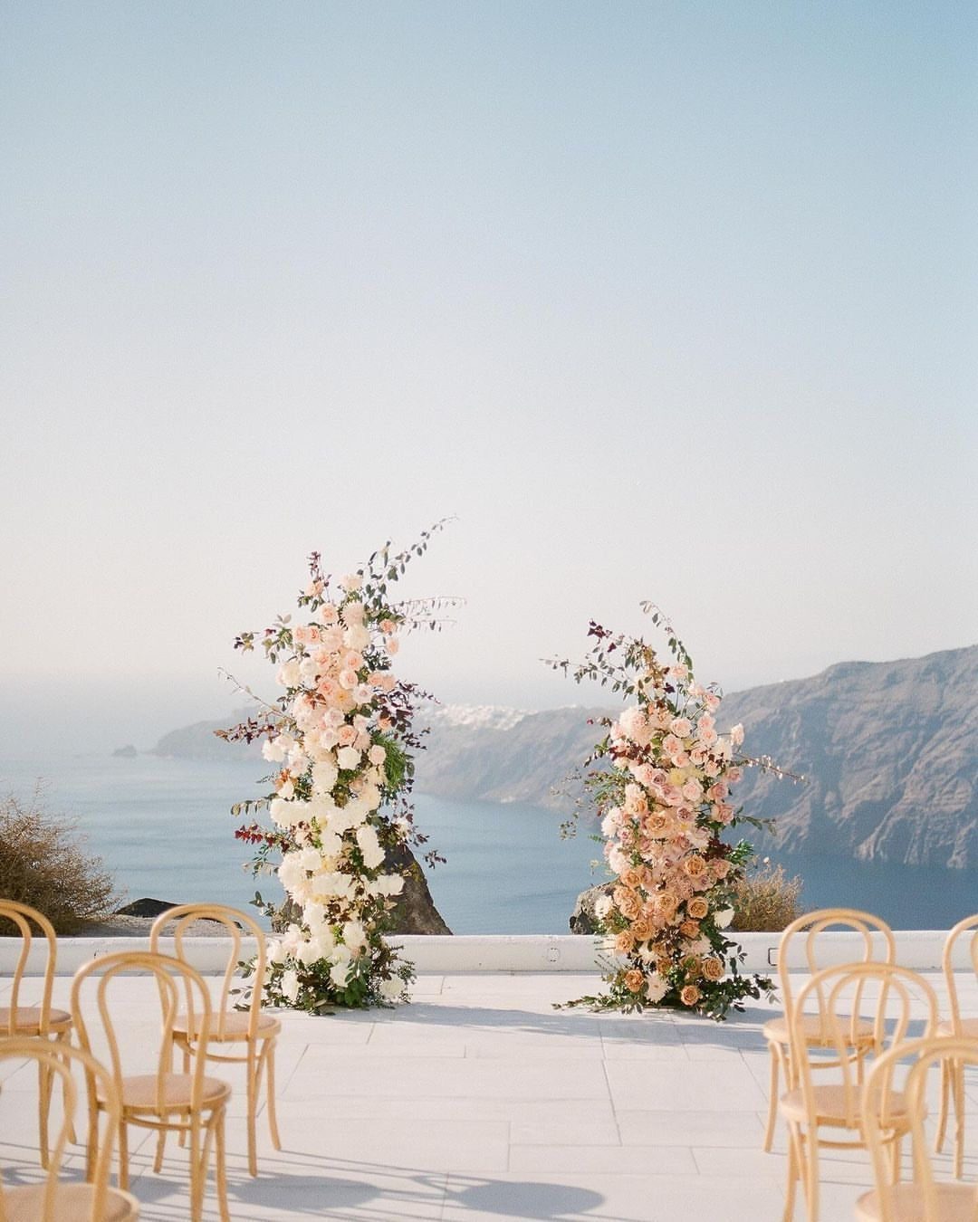 19 Wedding Backdrop Decorations for Any Ceremony Style 6 Two asymmetrical floral pillars with pink and white roses overlooking a coastal cliff landscape.