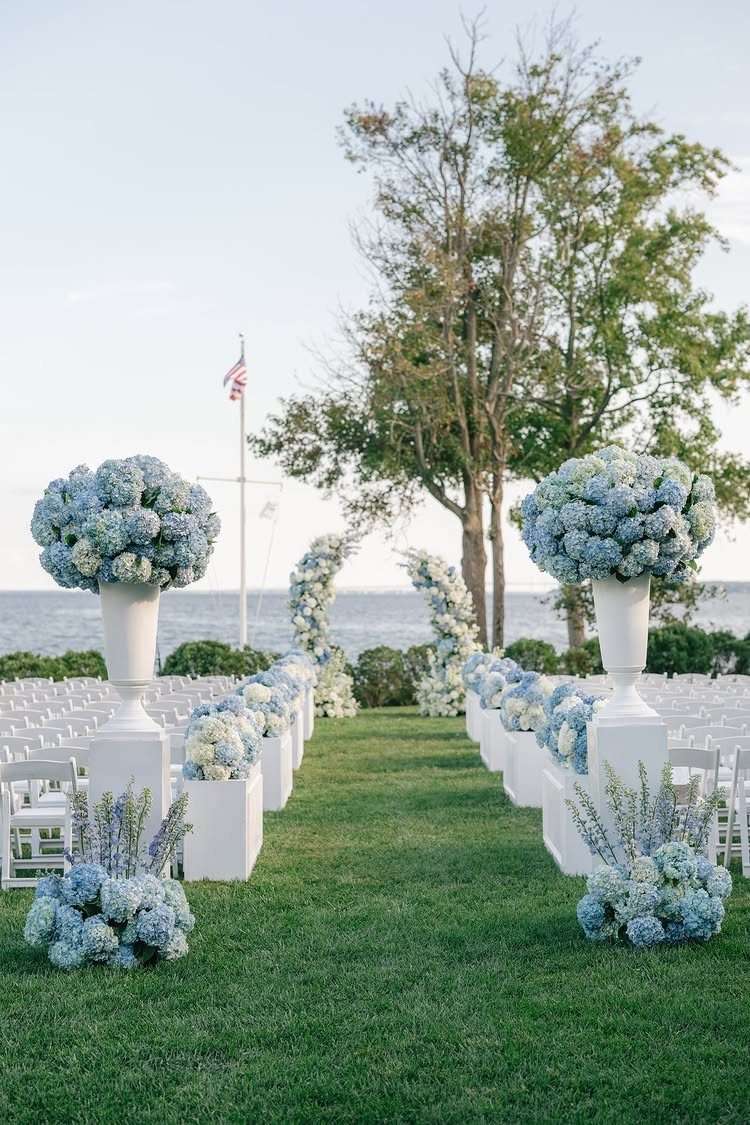 19 Wedding Backdrop Decorations for Any Ceremony Style 7 Blue and white floral arches and hydrangea arrangements lining a grassy wedding aisle