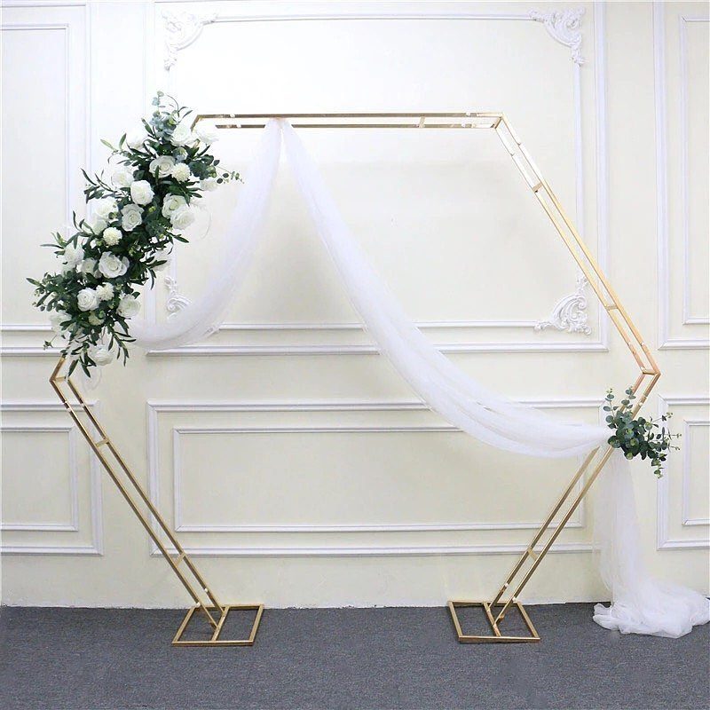 19 Wedding Backdrop Decorations for Any Ceremony Style 1 Gold hexagonal wedding arch with white floral arrangements and draped white sheer fabric.