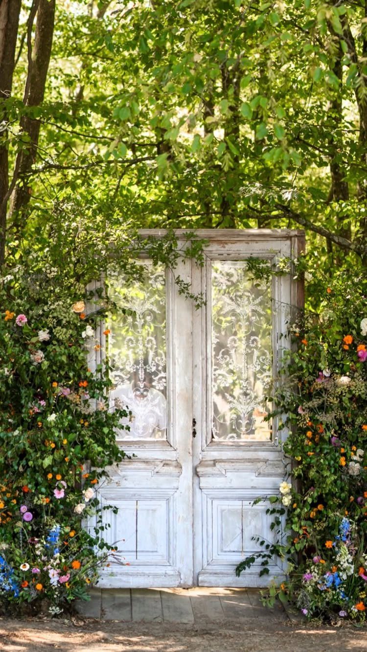 19 Wedding Backdrop Decorations for Any Ceremony Style 2 Vintage white wooden doors framed by colorful flowers and green leaves in a garden.