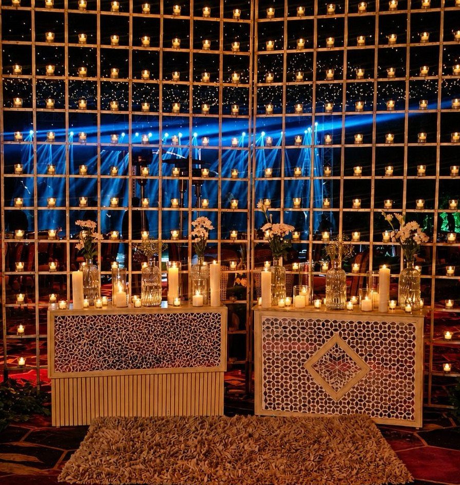 19 Wedding Backdrop Decorations for Any Ceremony Style 8 Gold grid wall filled with glowing candles behind floral table arrangements and blue lighting.