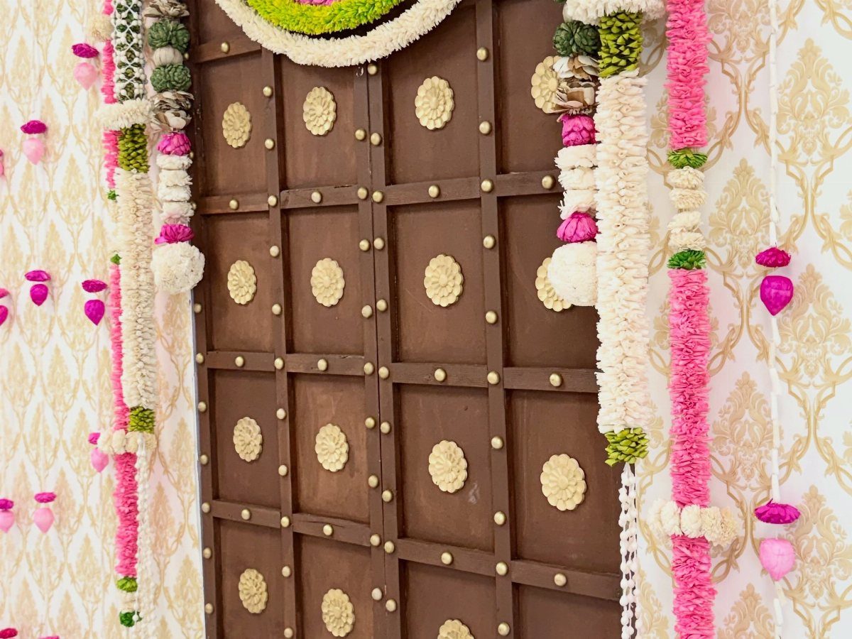 19 Wedding Backdrop Decorations for Any Ceremony Style 19 Brown wooden paneled wall adorned with colorful floral garlands and gold patterned wallpaper.