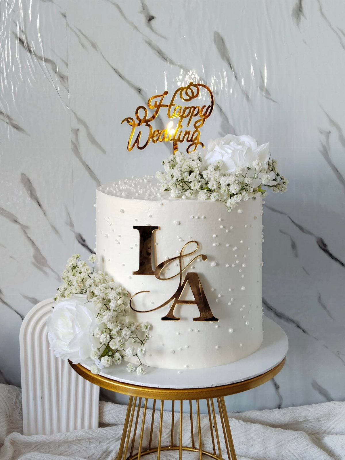 White wedding cake with gold initials and flowers on a gold stand