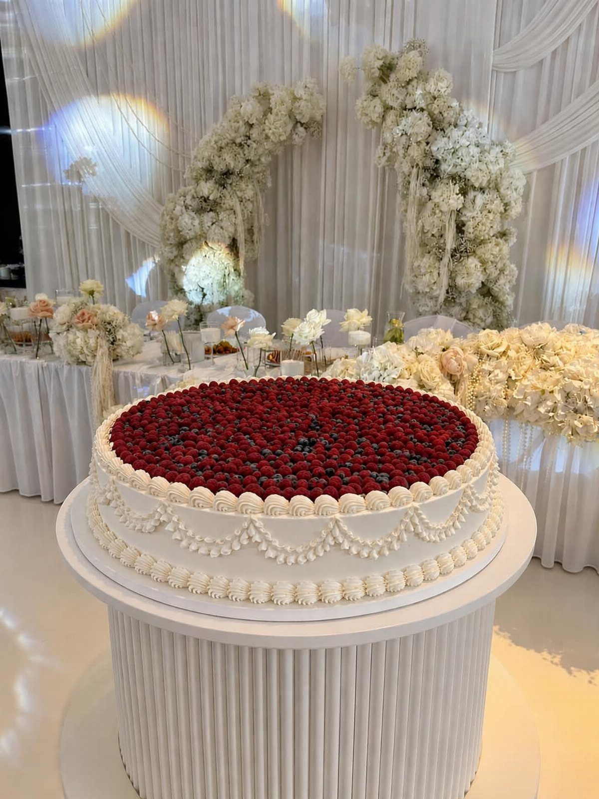Round white cake topped with raspberries and blueberries on a white fluted pedestal