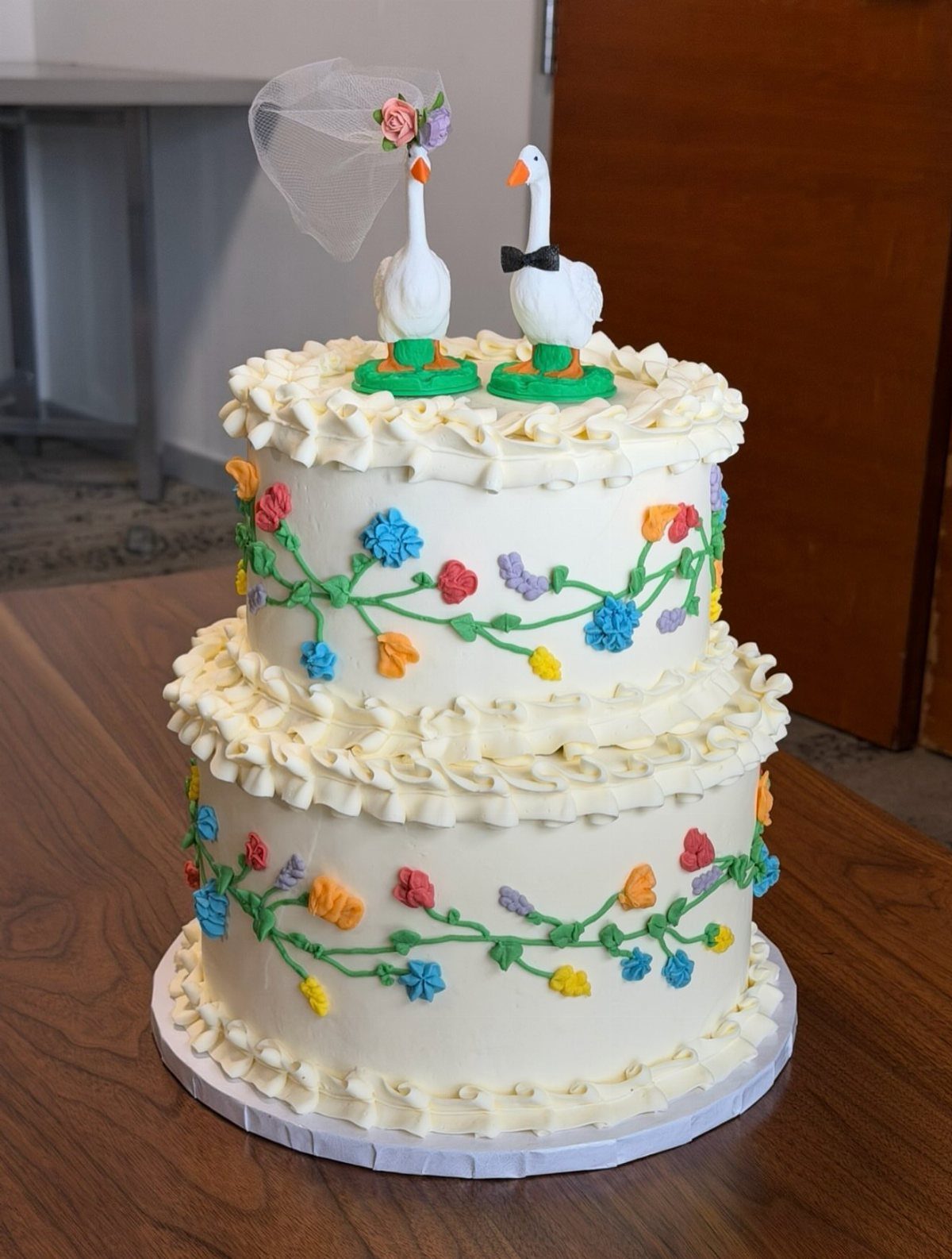 Wedding Cake Photo Ideas: 6 Designs for Every Style 3 Two-tier white wedding cake with colorful flowers and goose figurines on top.