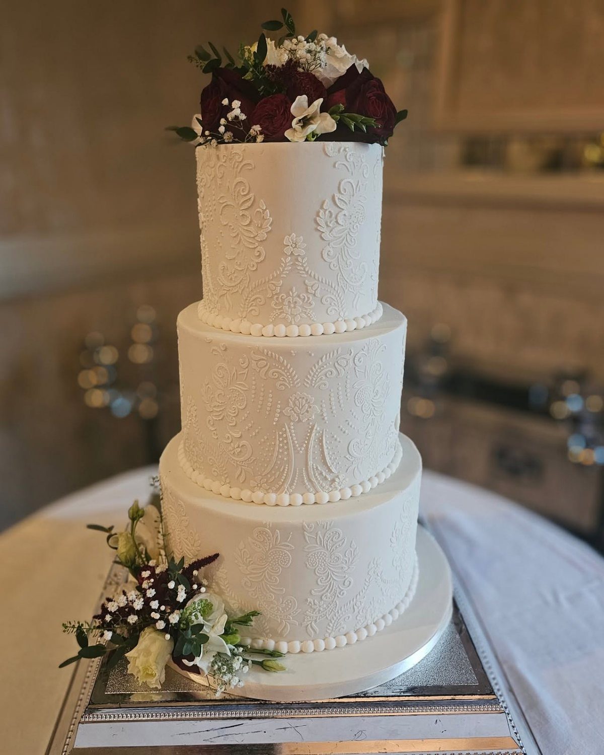 Wedding Cake Photo Ideas: 6 Designs for Every Style 2 Three-tier white wedding cake with intricate lace piping and red rose floral toppers.