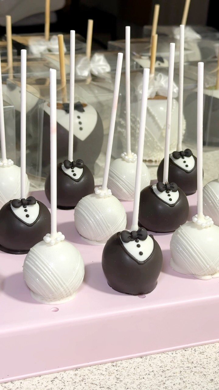 5 Wedding Cake Pops Ideas for Favors and Dessert Tables 3 Tuxedo and white drizzled cake pops arranged on a pink display tray.