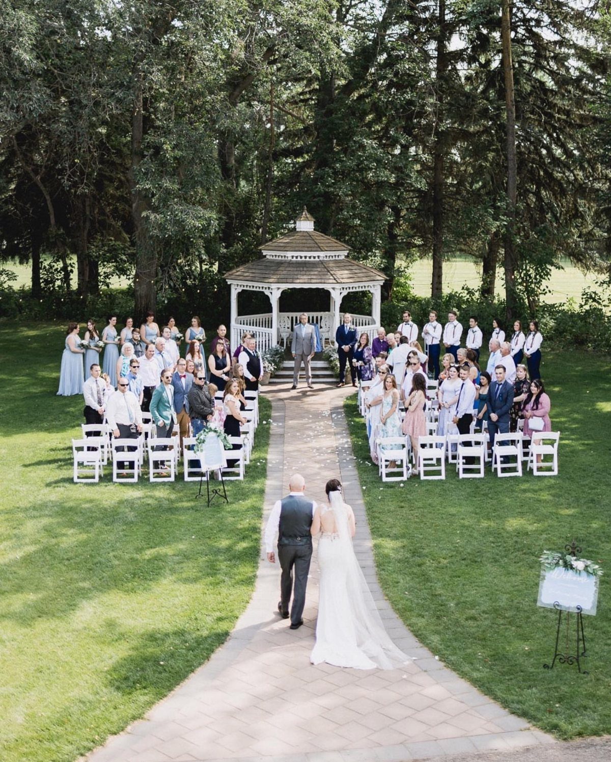 Bride and groom walking toward a white gazebo altar during an outdoor wedding ceremony.