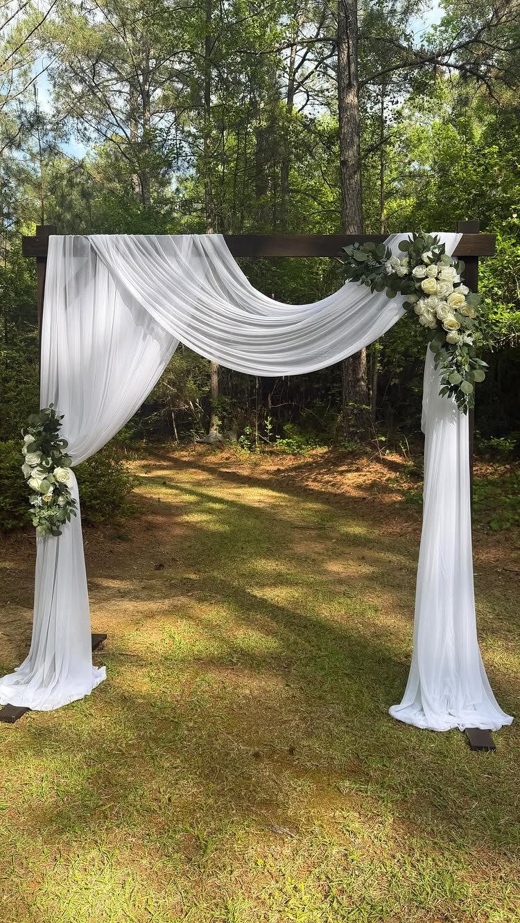 Wooden wedding altar with white fabric draping and flowers in a forest setting